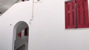 Un edificio blanco con un persiano rojo, una puerta blanca y una barandilla negra en una escalera.