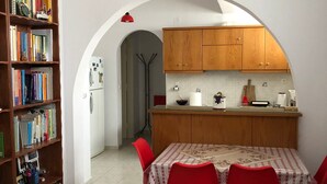 Un comedor con una mesa dispuesta para cuatro personas, rodeado de sillas rojas, una estantería llena de libros y una cocina visible a través de un arco.