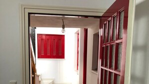 Un pasillo con una puerta roja, paredes blancas y una escalera que lleva a otra habitación.