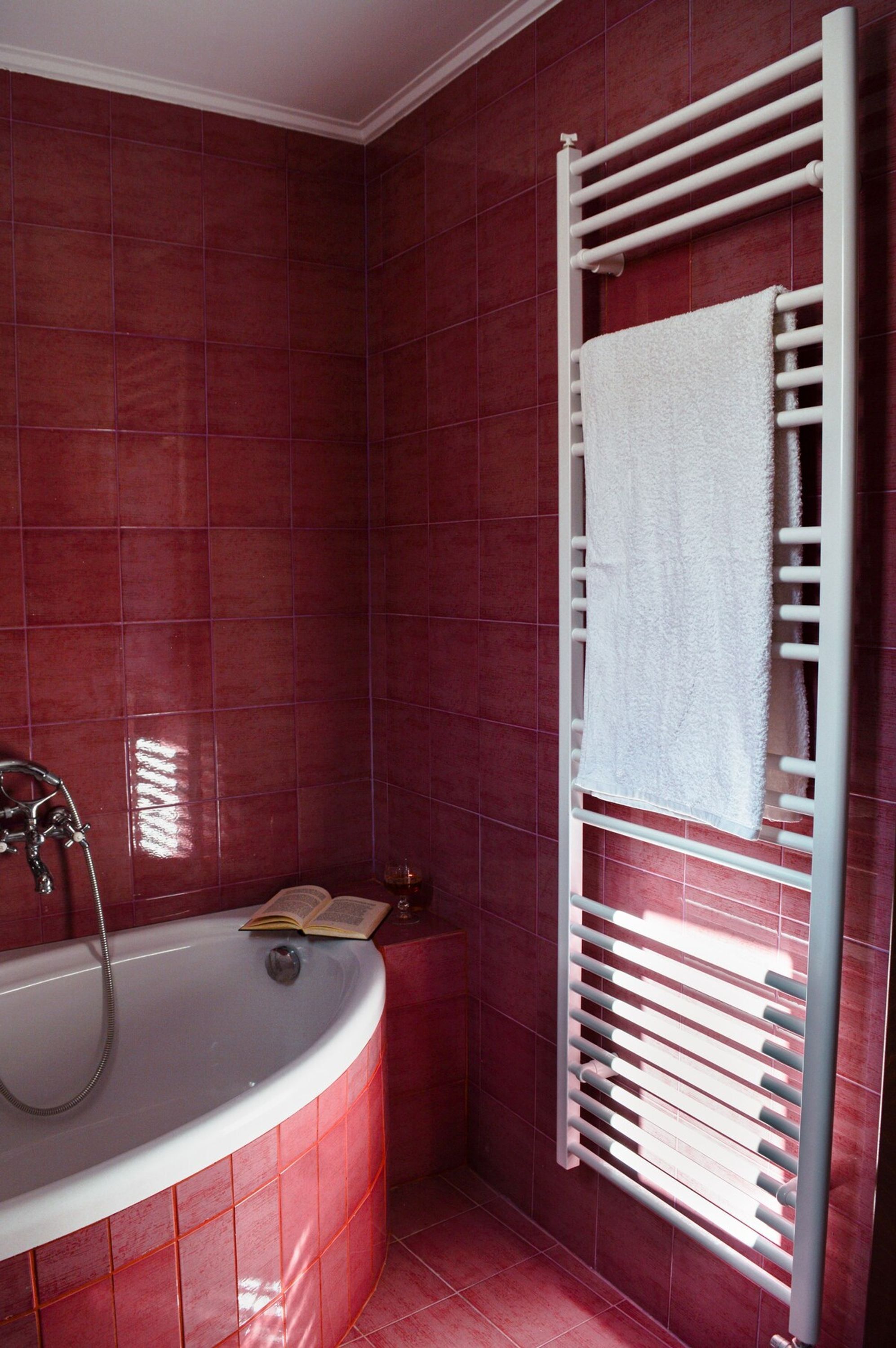 A bathroom with a white bathtub, a white towel hanging on a rack, and red tiled walls.