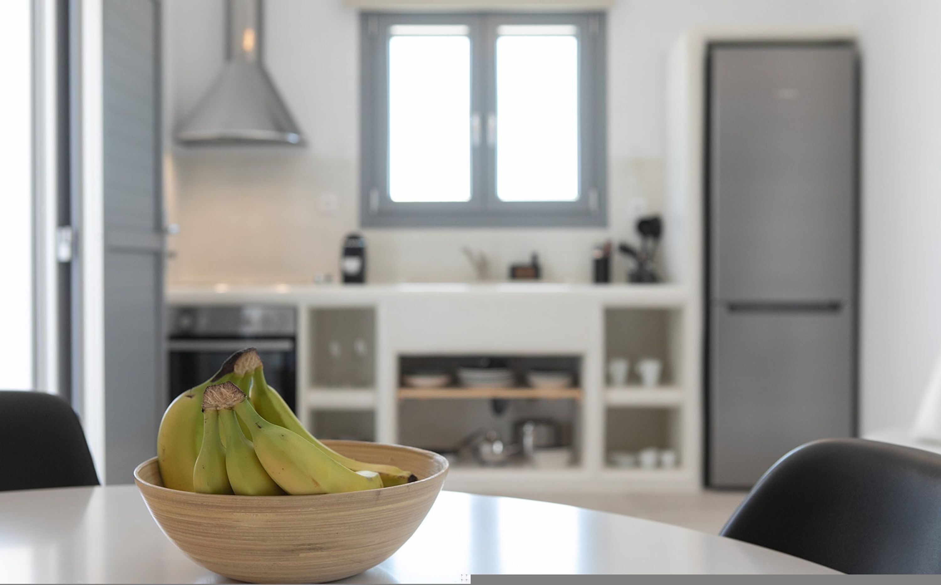 A modern kitchen with a wooden bowl of bananas on a table.