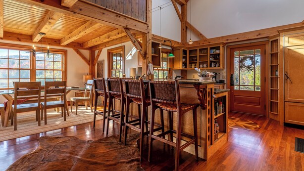 A rustic interior with wooden beams, a bar area, and a dining space with chairs and a rug.