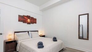 Habitación de hotel con cama, mesitas de noche, espejo montado en la pared y una obra de arte con atardecer.