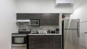 Una cocina compacta con armarios de madera oscura, un refrigerador de acero inoxidable, un microondas, una estufa y una cafetera.