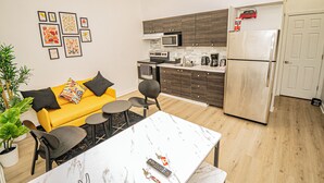 Una cocina moderna con microondas, estufa y refrigerador. Hay un sofá amarillo con cojines negros y una pequeña mesa de comedor con sillas.