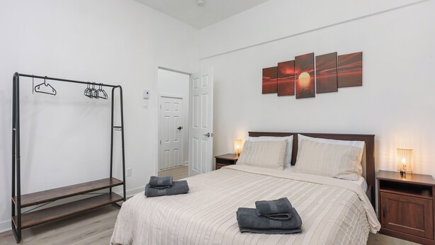 Un dormitorio con cama, armario de madera, perchero y una obra de arte colgada en la pared.