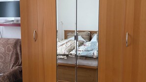 Ein Zimmer mit einem Holzschrank, einem Bett mit gemusterten Textilien und einem Fernseher auf einem Schrank.