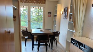Ein Essbereich mit Holztisch und -stühlen, eine Küche mit Holzschrank sowie Blick auf Bäume durch das Fenster.