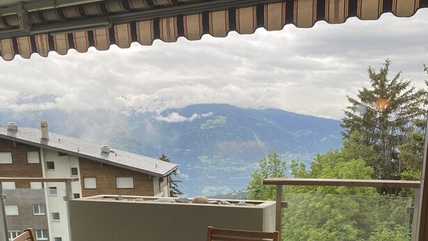Ein Balkon mit Holztisch und Stühlen, einer roten Vase und einer Hasenfigur mit Sternenmuster.