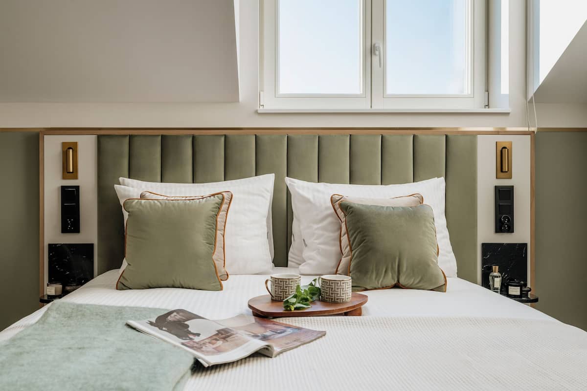 Un lit bien fait, avec une tête de lit recouverte d’un tissu vert, deux oreillers, un plateau avec deux tasses et un magazine posé sur le lit.