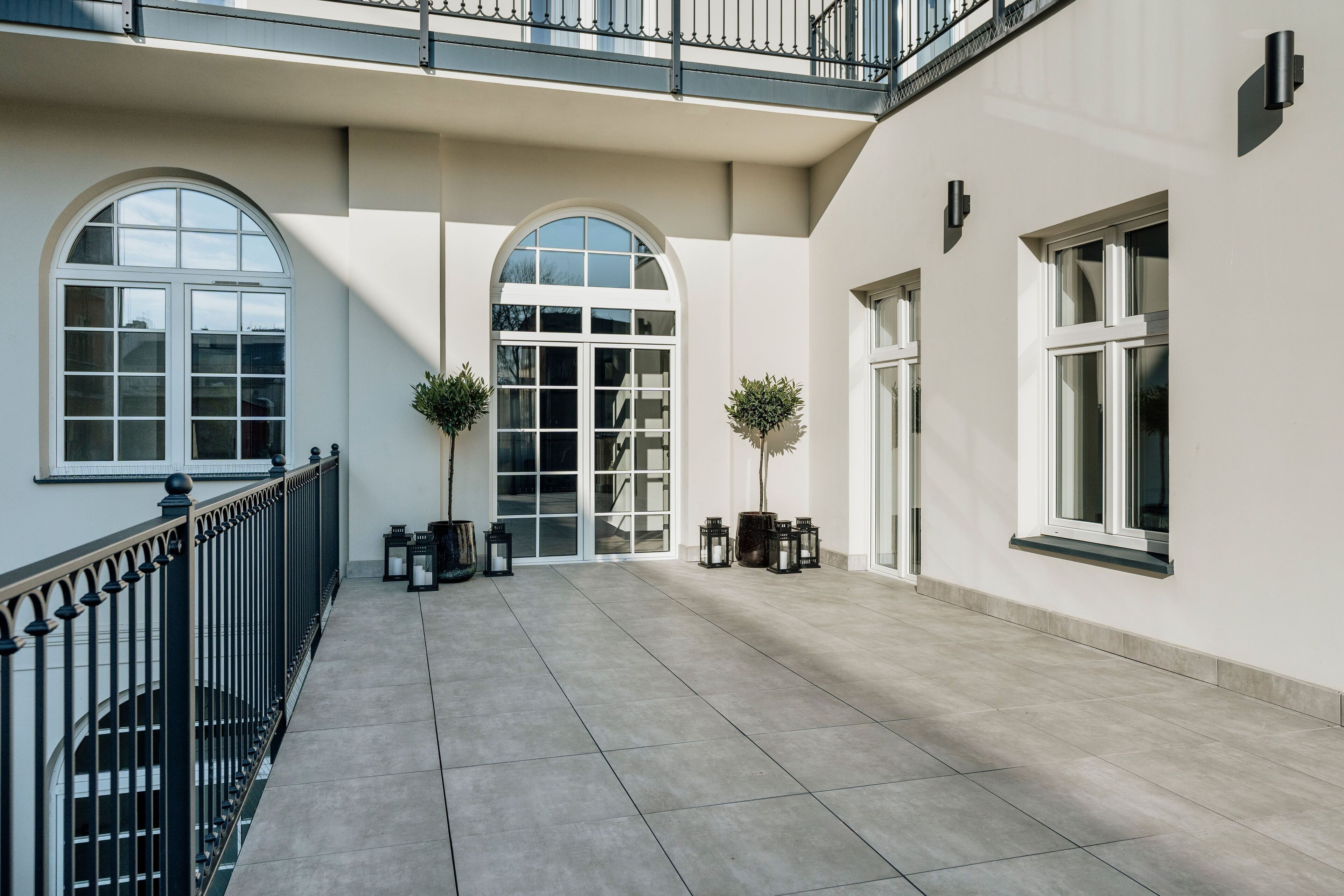 A spacious courtyard with a tiled floor, large arched windows, and a balcony with a railing.