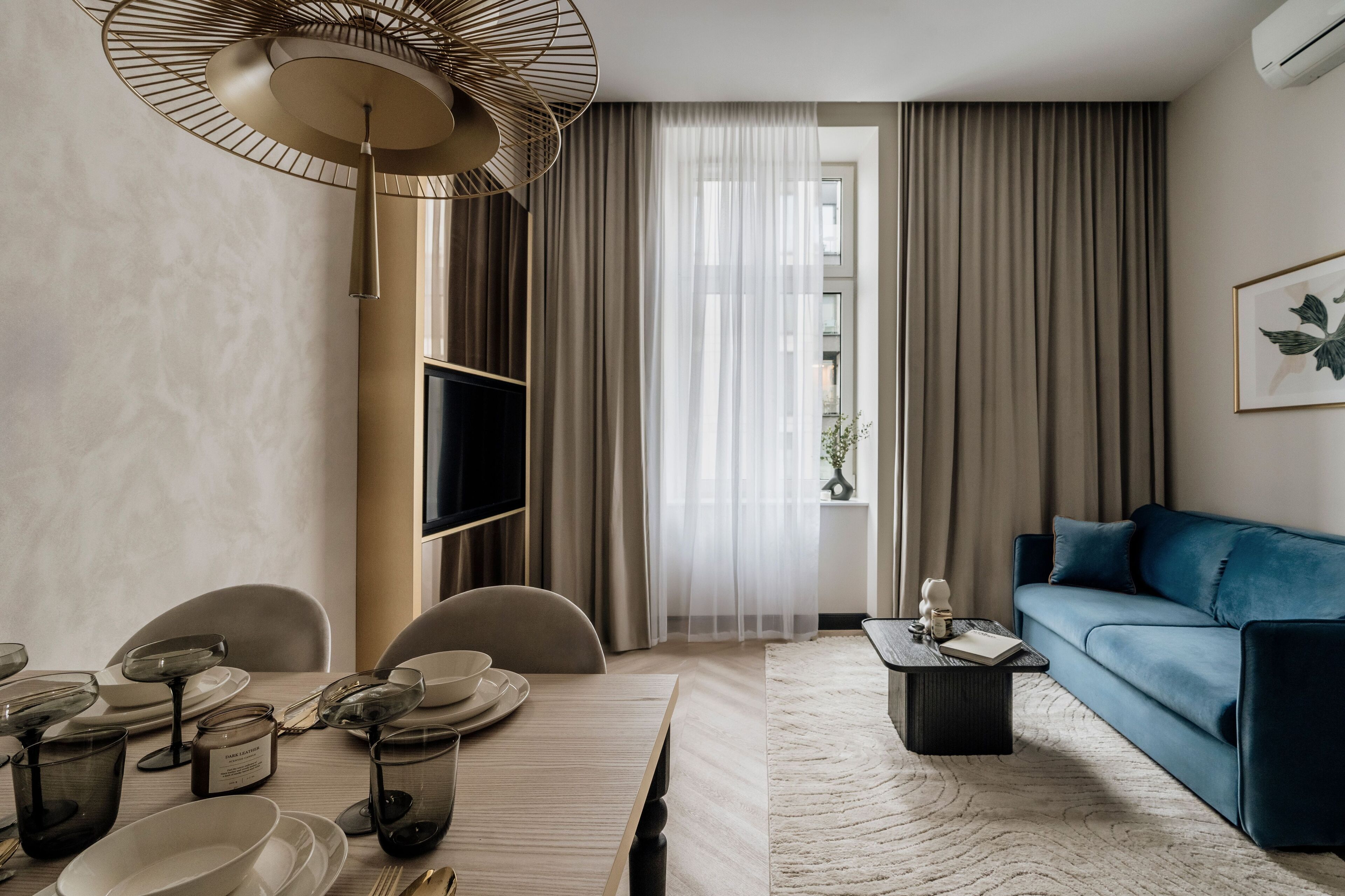 A modern living room with a dining area, a blue sofa, a flat-screen TV, and a large fan.