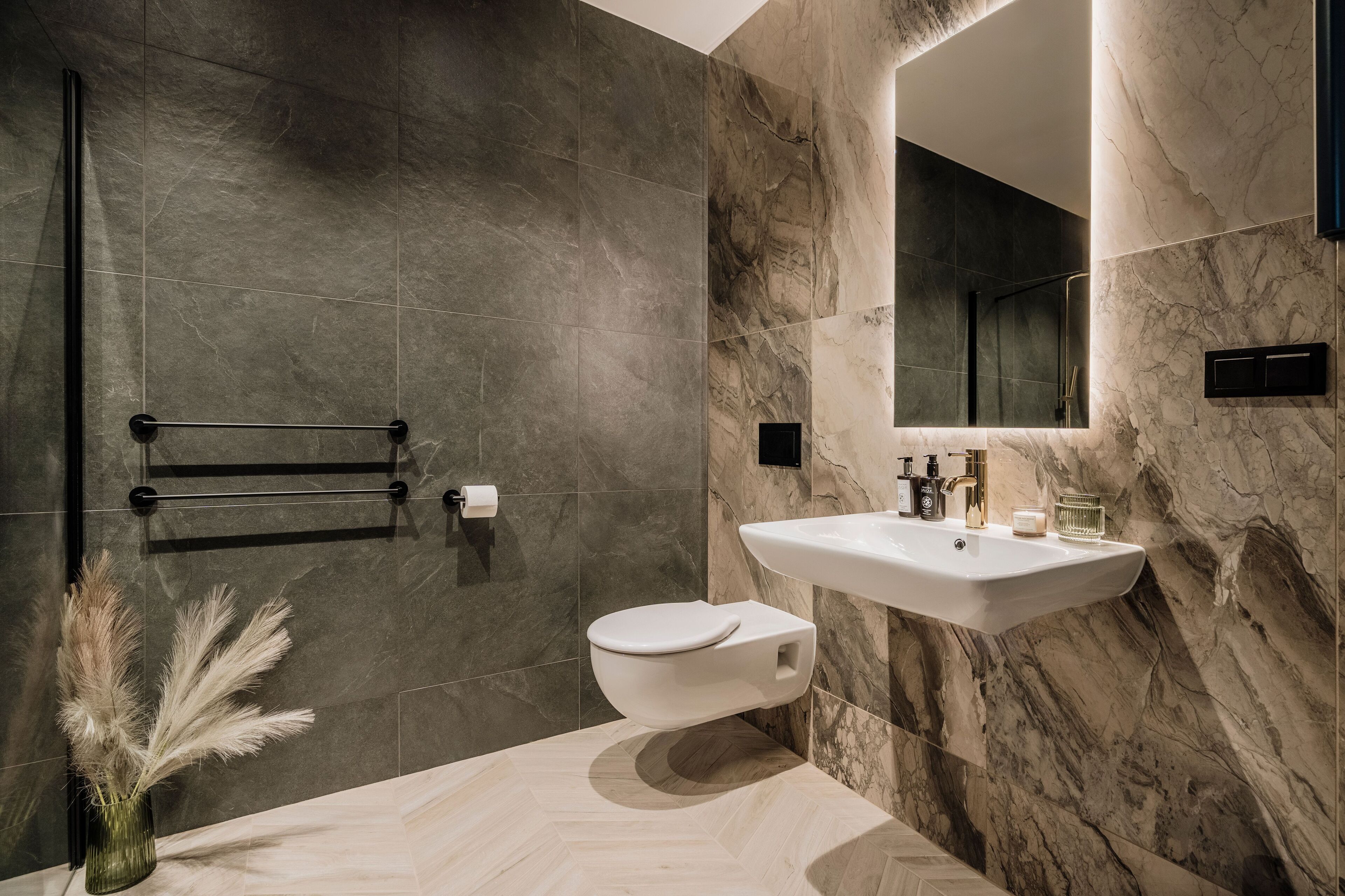 A modern bathroom with a marble wall, a white toilet, a sink with a mirror, and a towel rack.