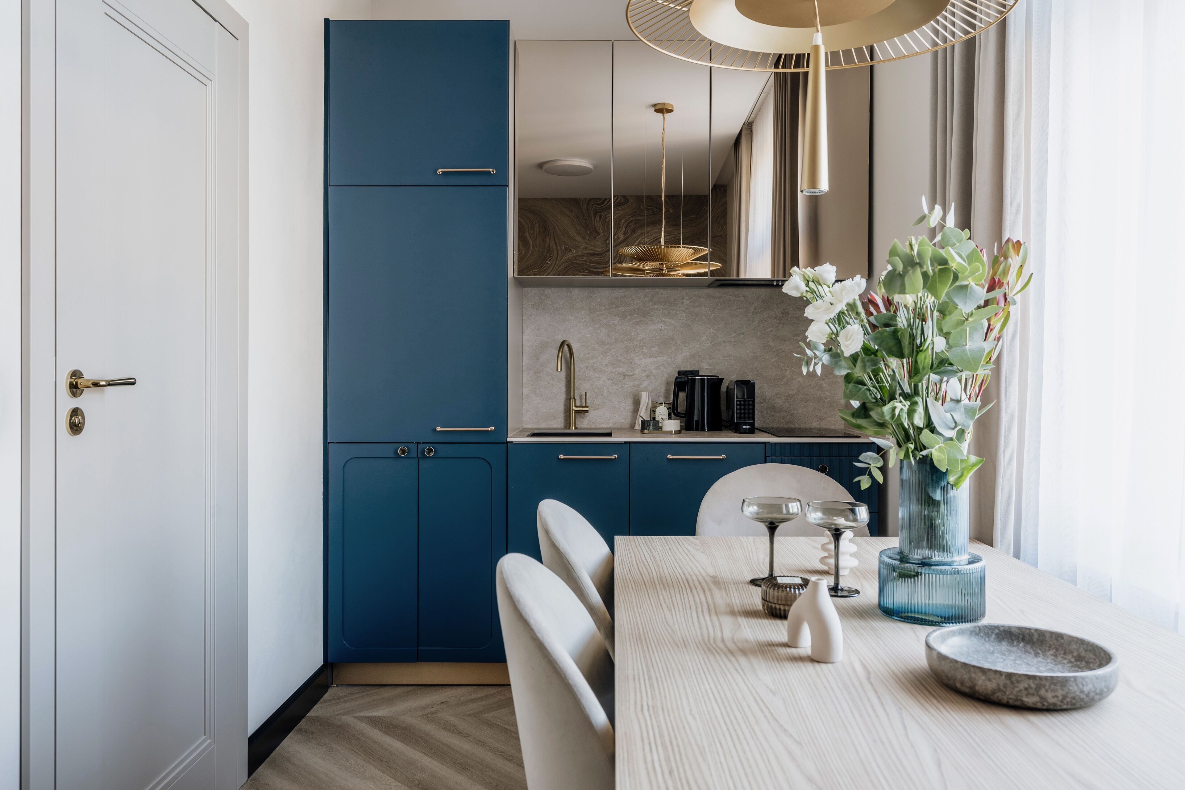 Une cuisine moderne avec des meubles de rangement bleus, une table à manger avec des chaises et un vase rempli de fleurs.