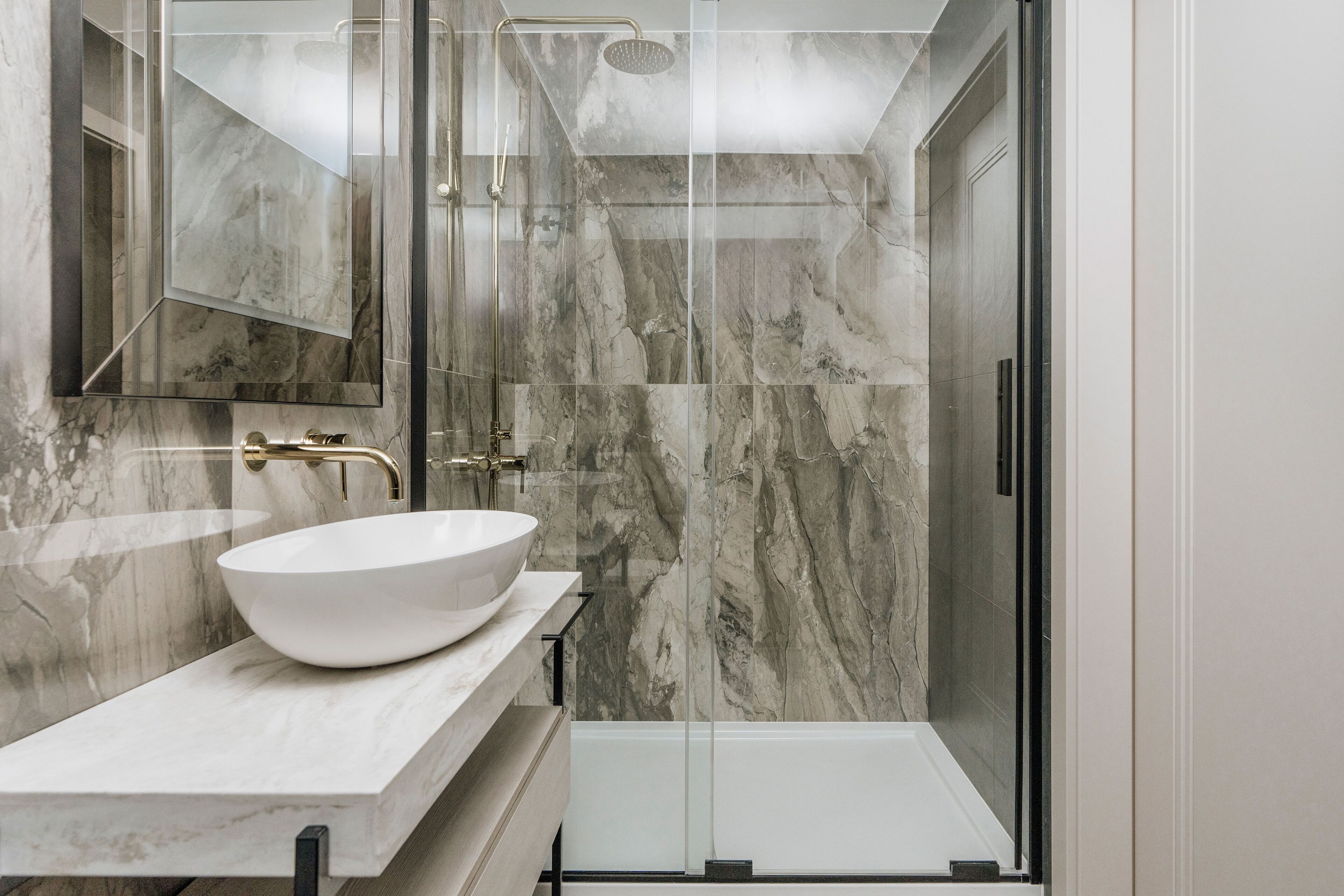 A modern bathroom with a marble vanity, a large mirror, and a glass-enclosed shower area.