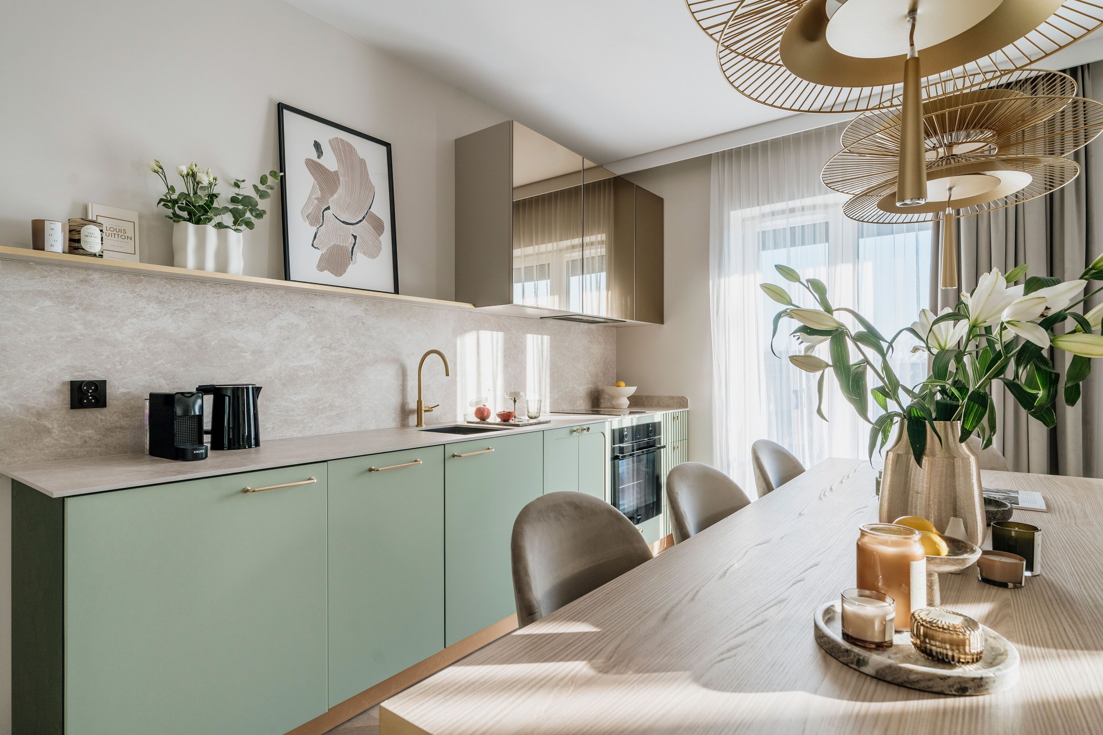 Een moderne keuken met een eethoek, met een lichtgekleurd aanrechtblad, groene keukenkastjes en een grote eettafel met stoelen.