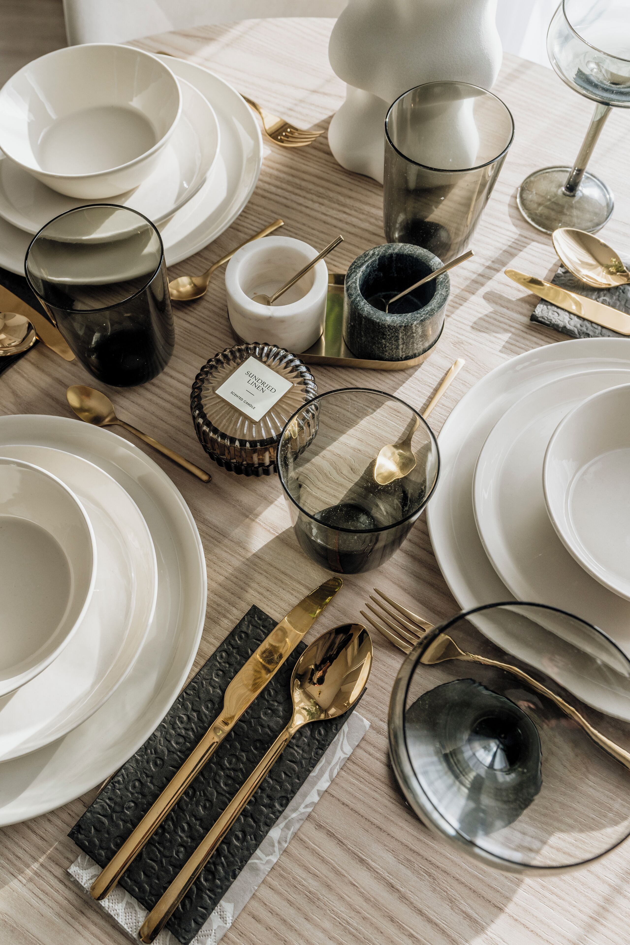 A table set with white plates, gold cutlery, and clear glassware.