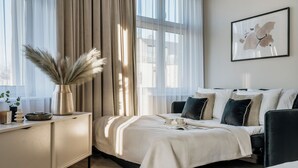 Un dormitorio moderno con cama, mesitas de noche, una lámpara de noche, un florero con plumas de pampa y una obra de arte enmarcada en la pared.