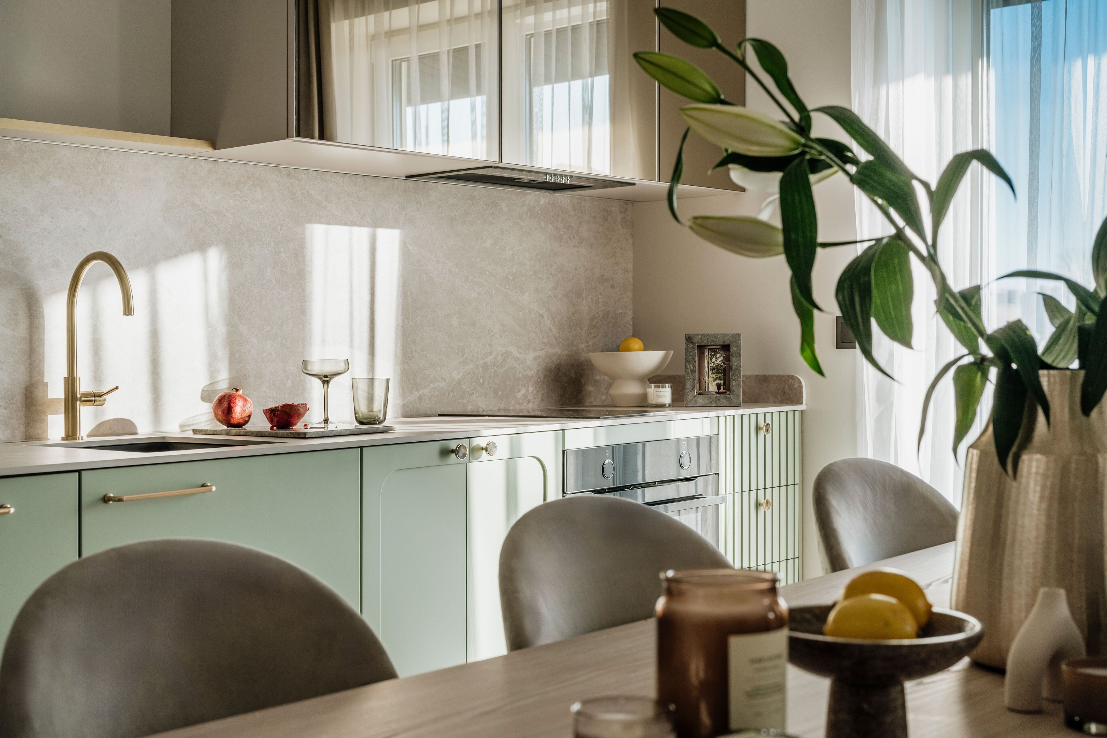 Een moderne keuken met een lichtgroen kleurenschema, een roestvrijstalen spoelbak en een eethoek met een houten tafel en stoelen.