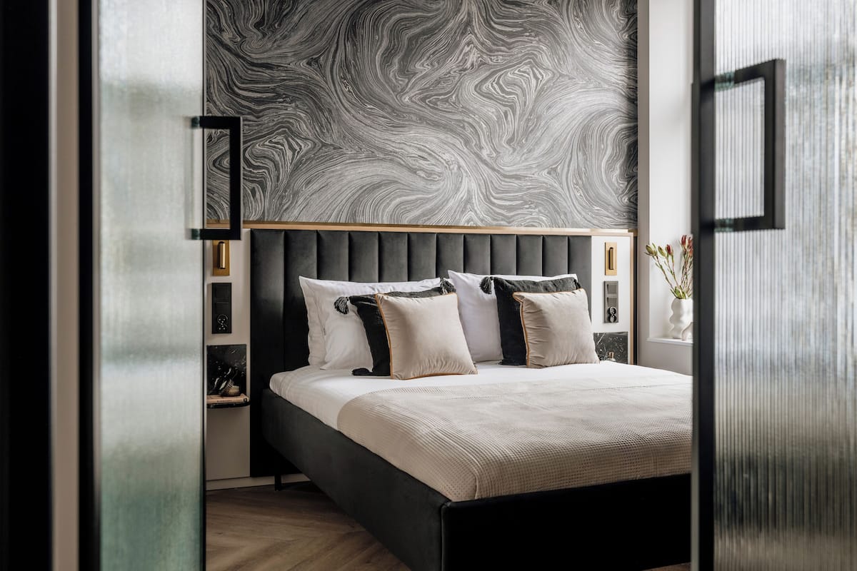 Une chambre à coucher moderne avec un grand lit, un mur décoré d’un motif imitant le marbre et un design minimaliste.