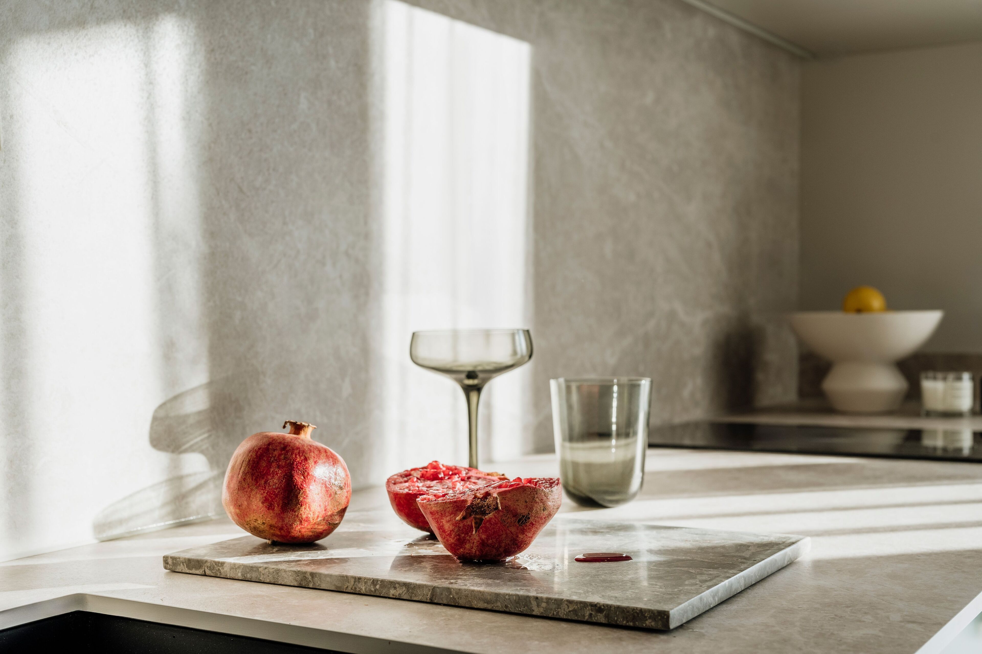 Un comptoir de cuisine avec une grenade, un verre à vin et un bol de fruits.