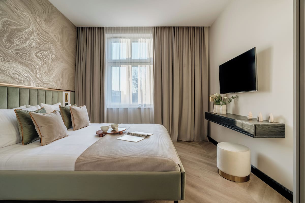 Une chambre d’hôtel moderne dotée d’un grand lit, d’un téléviseur à écran plat, d’une table de chevet agrémentée d’objets décoratifs et d’une fenêtre avec des rideaux.