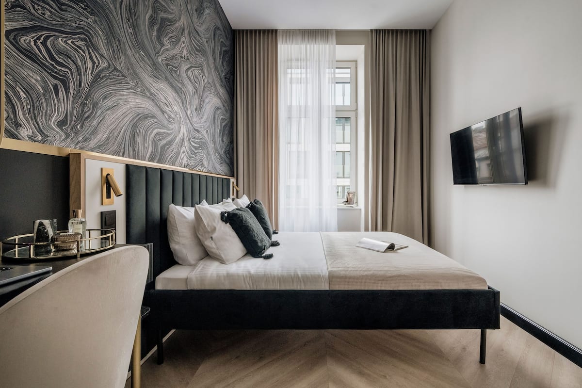 Une chambre d’hôtel moderne équipée d’un lit, d’une table de chevet, d’une télévision et d’une grande fenêtre avec des rideaux.