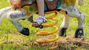 Een kindje op een stilstaand, paardvormig speeltoestel in een park.