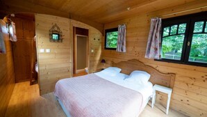 Een houten slaapkamer met een bed, een nachtkastje, een kledingkast en een raam met gordijnen.