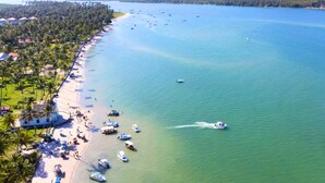 A beach with boats, a jet ski, and a row of houses along the shore. - Eco Resort Praia dos Carneiros  (Tamandaré)