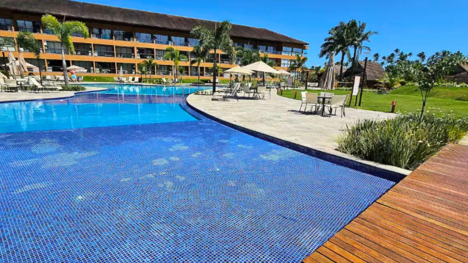 Ein Hotelpoolbereich mit klarem, blauem Wasser, Liegestühlen und einer Holzterrasse.