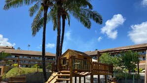 A playground with a slide and climbing structure, surrounded by palm trees and a building with multiple windows. - Eco Resort Praia dos Carneiros  (Tamandaré)