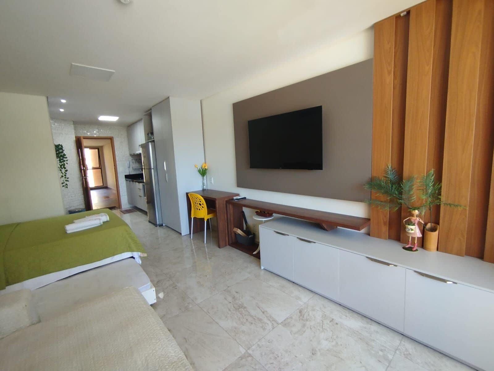 A modern hotel room with a bed, a desk, a flat-screen TV, and a kitchenette.