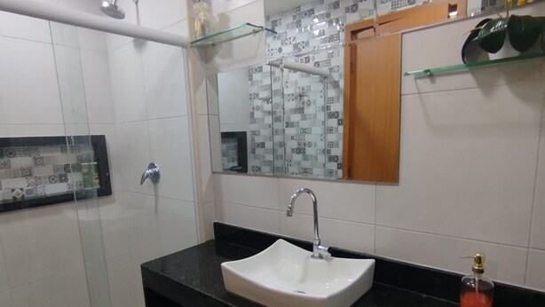 A modern bathroom with a glass shower enclosure, a white sink, and a mirror with a decorative backsplash. - Eco Resort Praia dos Carneiros  (Tamandaré)