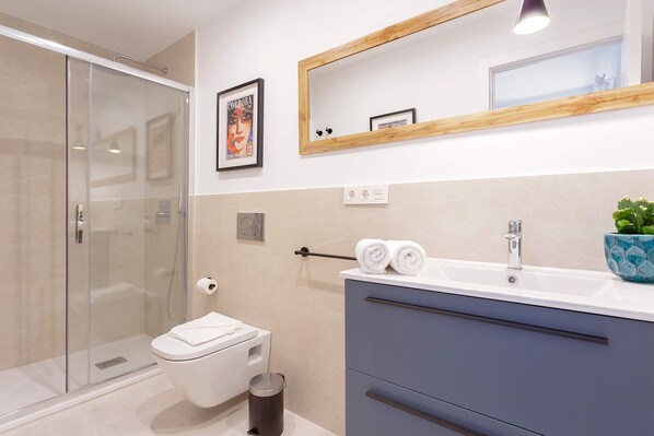 A modern bathroom with a glass shower enclosure, a toilet, a sink with a mirror, and a blue decorative pot.