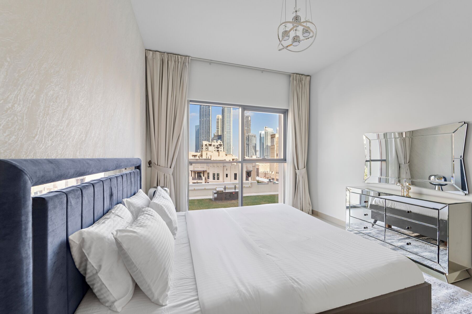 Une chambre d’hôtel moderne dotée d’un grand lit, d’une coiffeuse avec miroir et offrant une vue sur le paysage urbain grâce à une grande fenêtre.