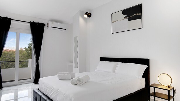 A modern bedroom with a large bed, a bedside table with a light, a window with curtains, and a wall-mounted air conditioner. - #266 Luxurious Villa Bellagio by Home Holidays (Albufeira)