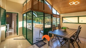 A modern home with a glass-enclosed patio, a dining area with a table and chairs, and a wooden ceiling.