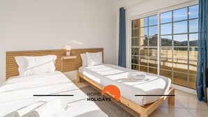 A bedroom with two beds, a large window with a view, and a wooden headboard.