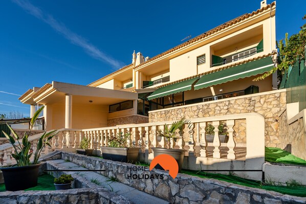 A two-story house with a stone facade, a balcony with green awning, and potted plants.