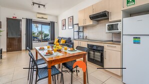 A modern kitchen with a microwave, oven, and a refrigerator. There is a dining table with chairs and a breakfast setup. - #253 Fernando Pessoa 26 by Home Holidays (Albufeira)