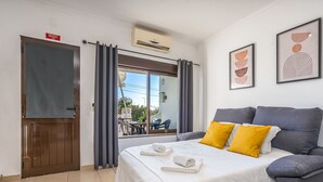 A hotel room with a bed, two pillows, a framed artwork, an air conditioning unit, a door, and a window with curtains. - #253 Fernando Pessoa 26 by Home Holidays (Albufeira)