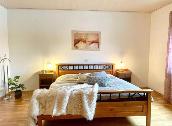 A bedroom with a wooden bed, two bedside tables, a wall-mounted painting, and a potted plant.