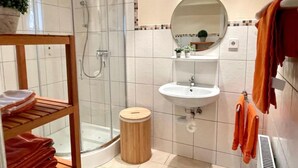 Un baño con cabina de ducha de vidrio, un estante de madera con toallas, un lavabo y un espejo.