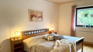 Un dormitorio con cama de madera, mesitas de noche, cortinas en la ventana y vistas a la vegetación exterior.
