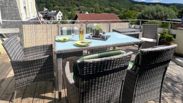 Una terraza de madera con muebles de mimbre y una mesa preparada para comer, con vista a un paisaje montañoso.