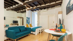 Una sala de estar moderna con un sofá color turquesa, una mesa de comedor con sillas, piso de madera y techo con vigas a la vista.