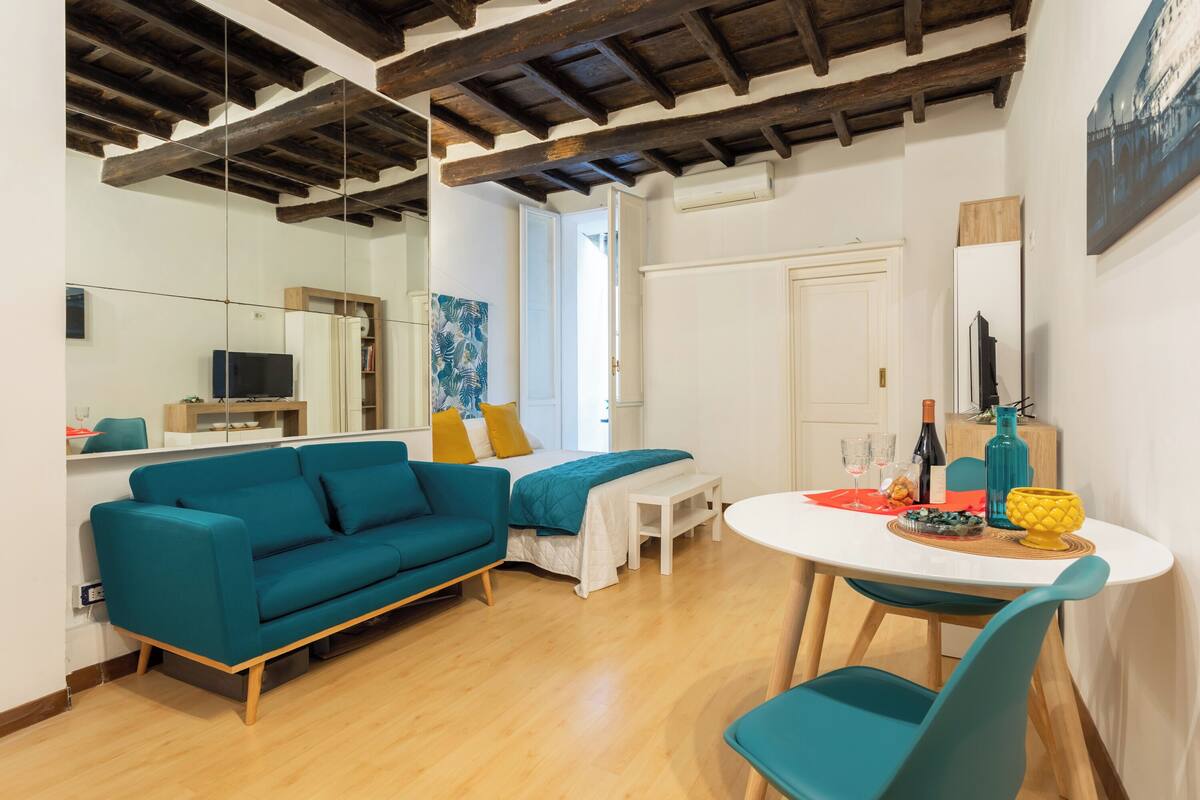 Un salon moderne avec un canapé de couleur turquoise, une table à manger avec des chaises, un plancher en bois et un plafond avec des poutres apparentes.
