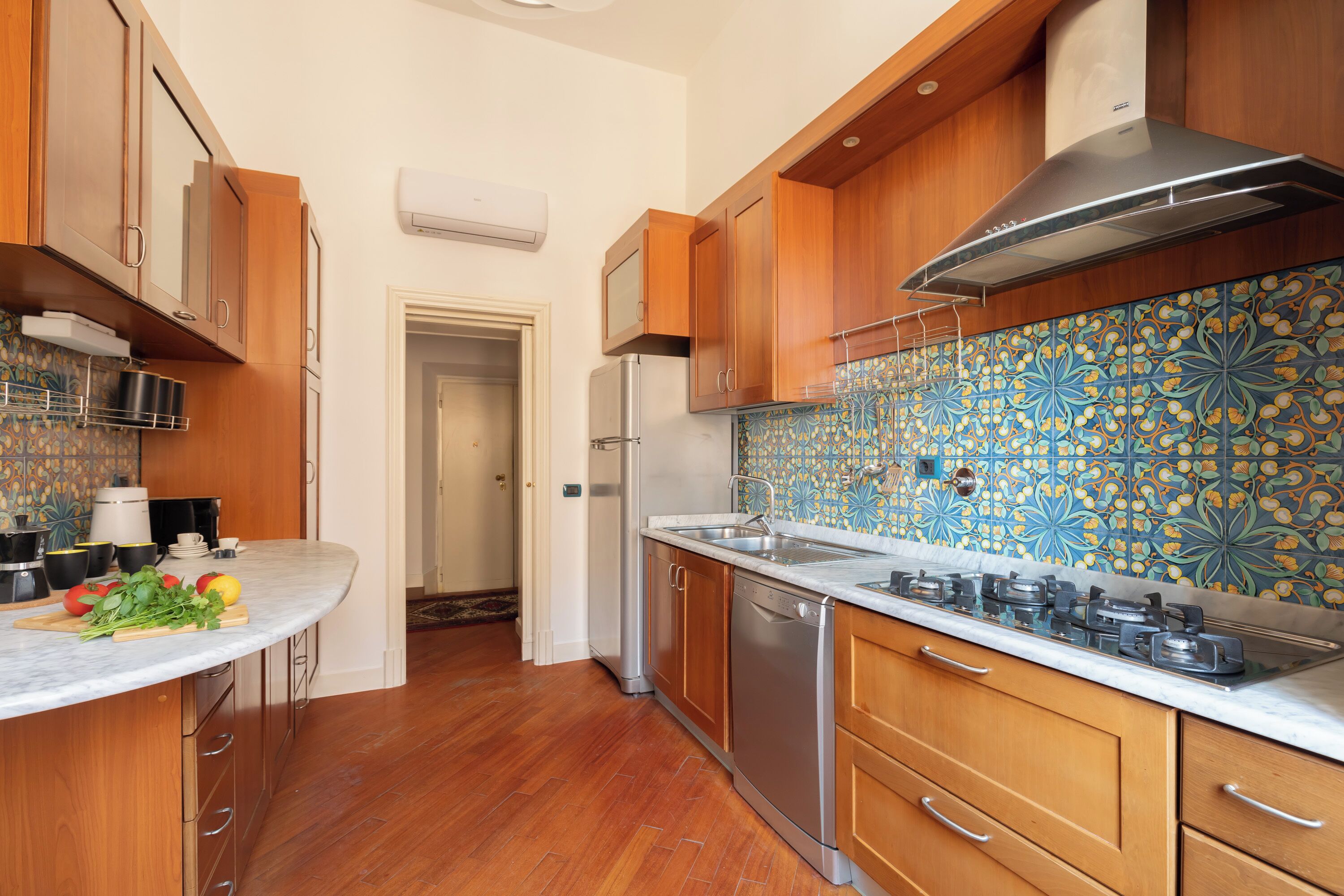 A kitchen with wooden cabinets, a stainless steel range hood, a tiled backsplash, and a marble countertop.