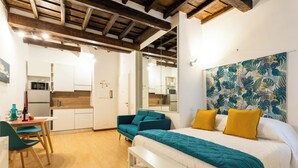 Una habitación compacta con cama, sofá, mesa de comedor y zona de cocina.